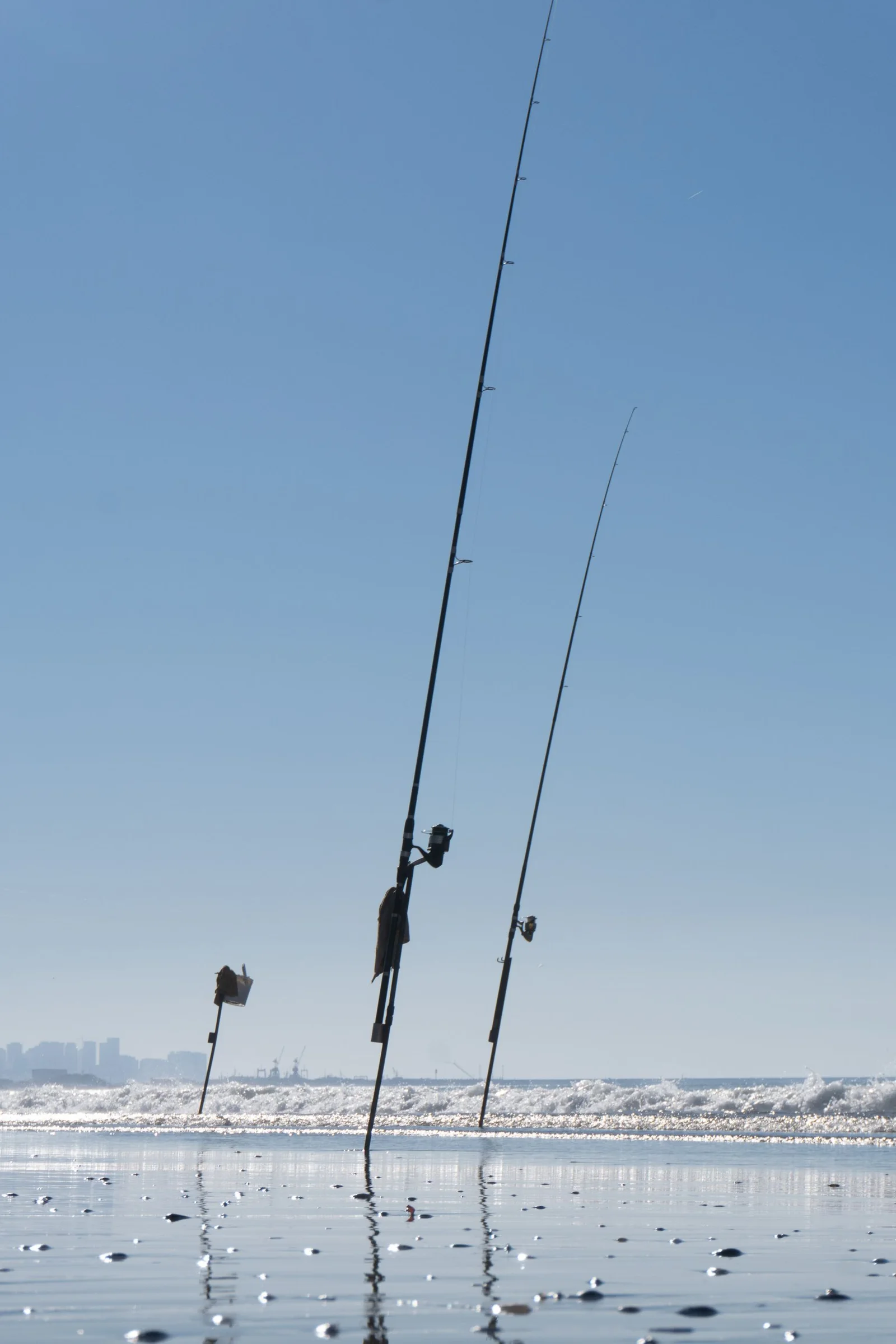 Fishing rods standing in sand beside the sea.