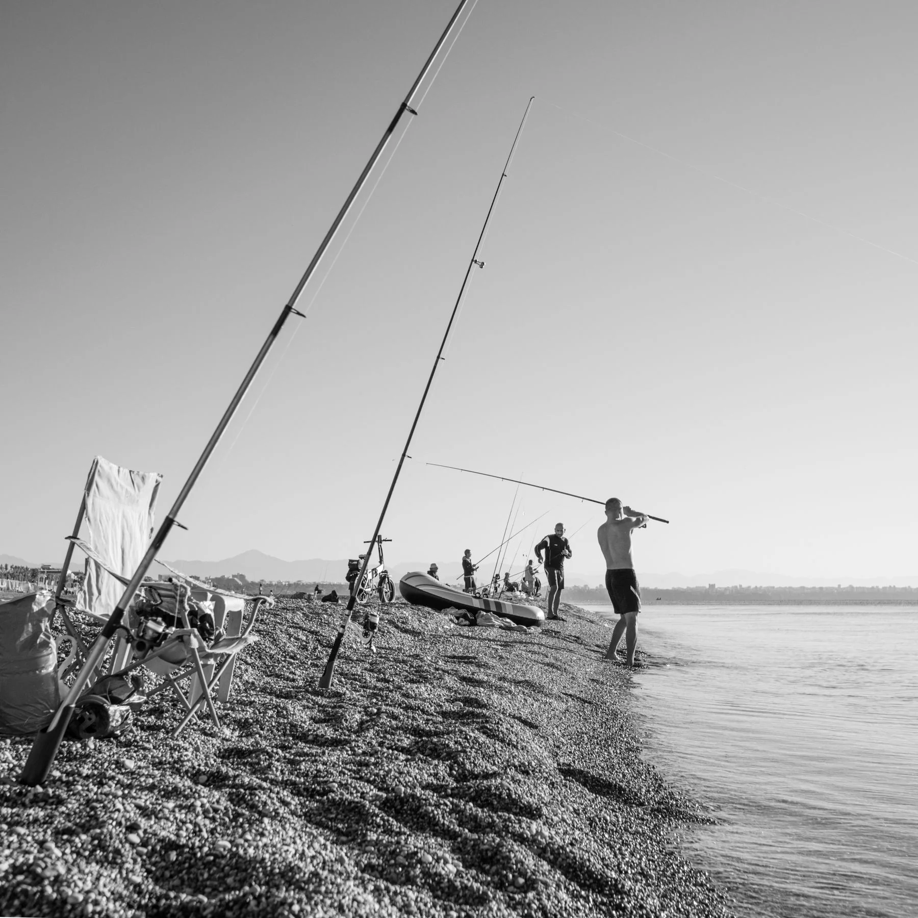 Black and white photograph of people fishing along a beach.